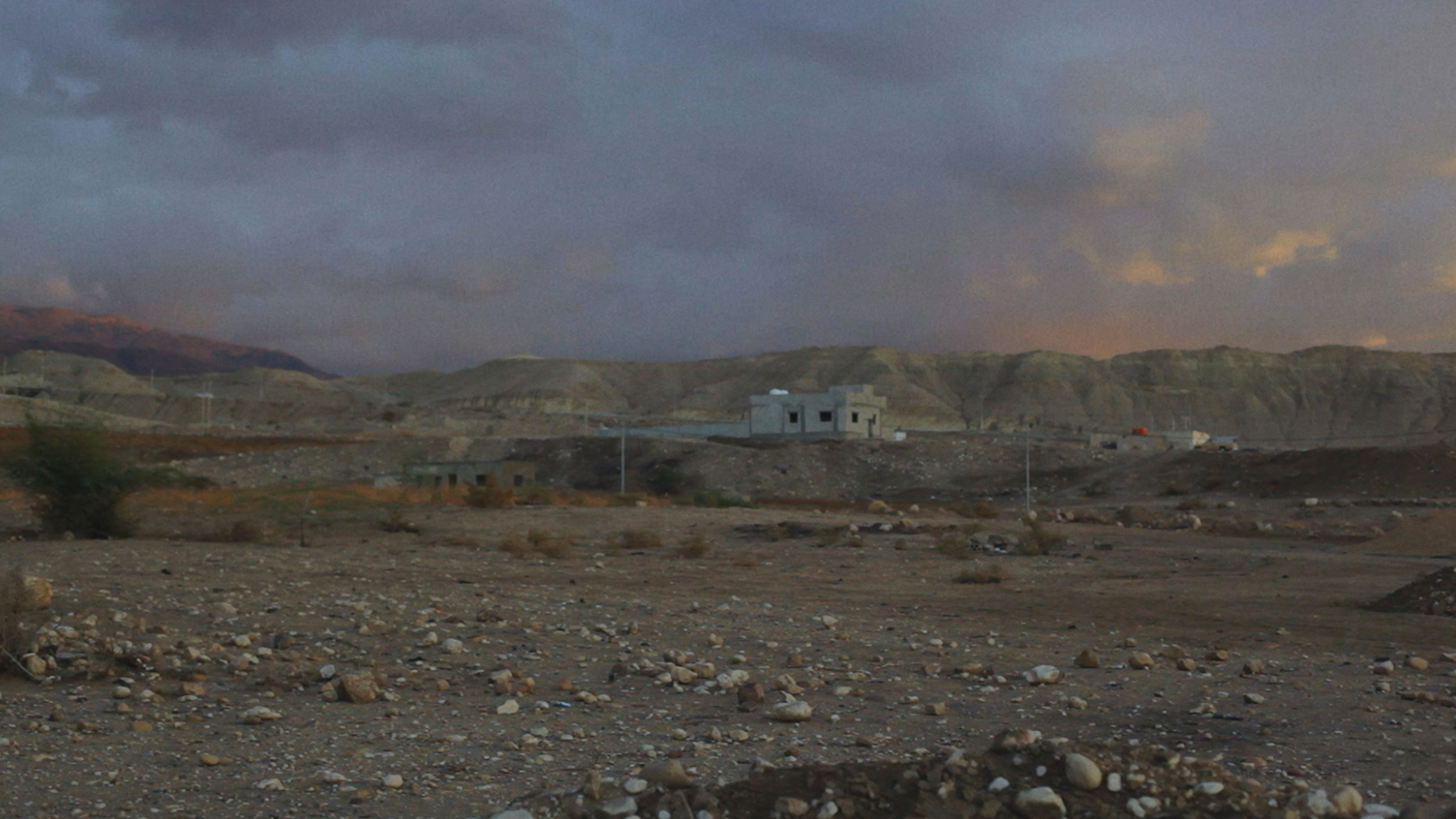En bar bygning i et øde ørkenlandskab med bjerge i horisonten, af Tore Hallas